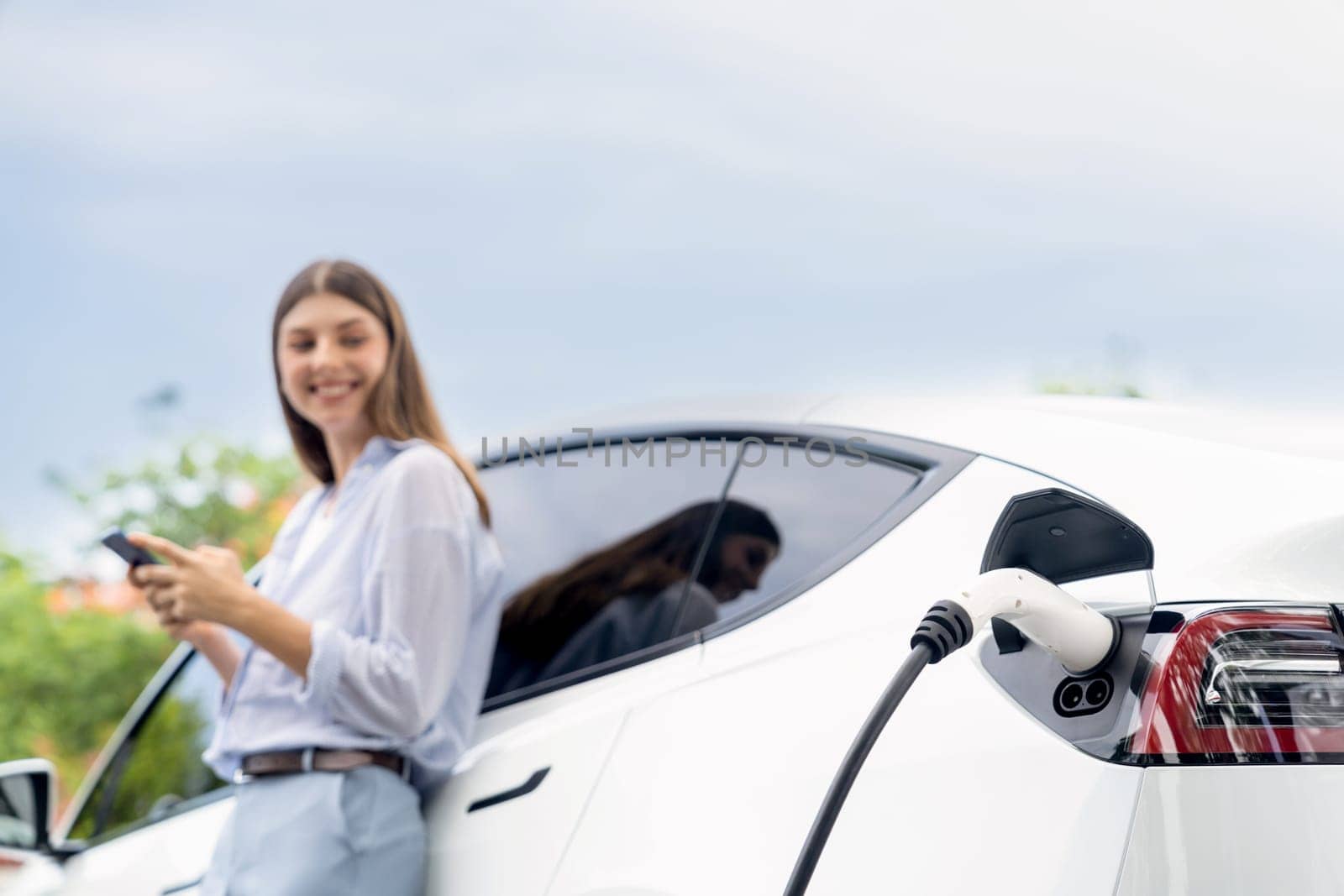 Young woman using smartphone to pay for electric car charging. Exalt by biancoblue