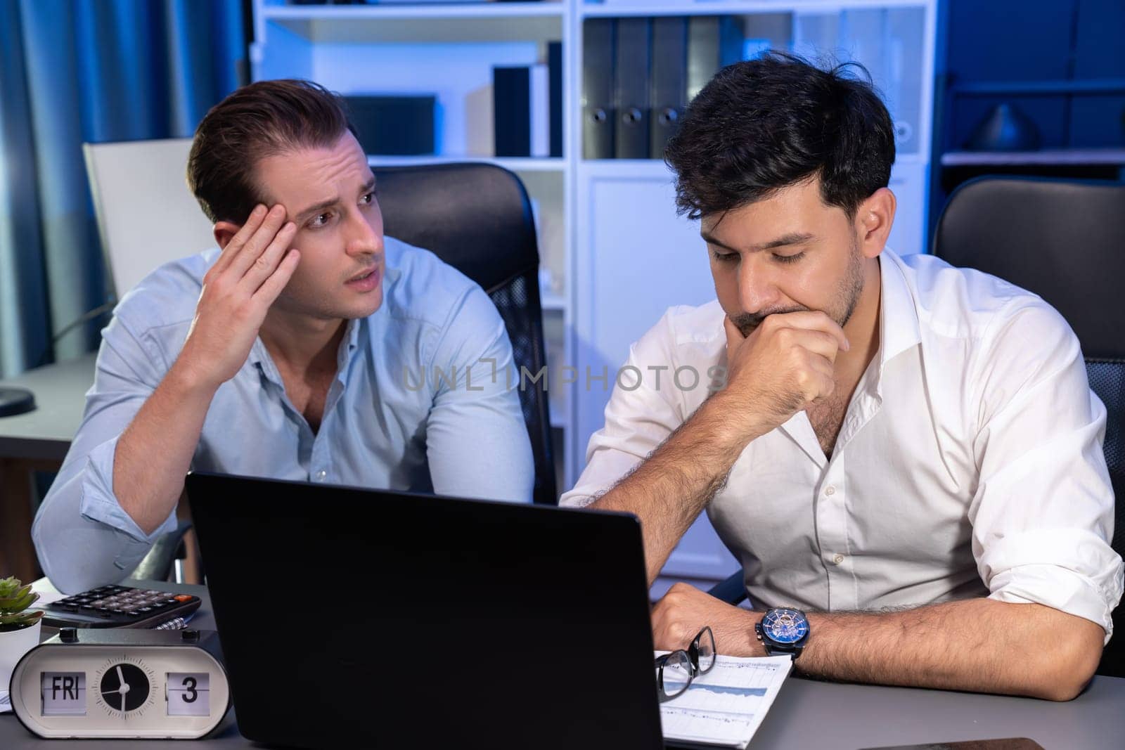 Stressful business partner with headache analyzing paperwork project together on desk at night time of startup product company. Concept of overworked design on neon blue light modern office. Sellable.
