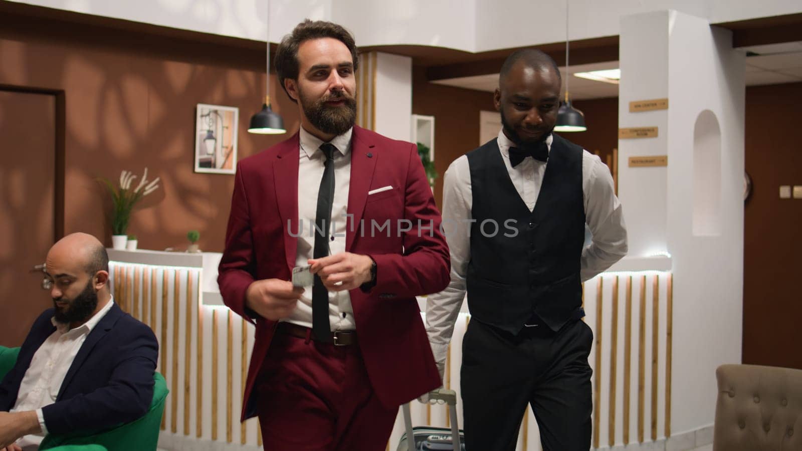 Gentleman getting access key card to enter room and relax while he is travelling on business trip. White collar worker in tailored suit at front desk lobby, hotel staff member welcoming client.