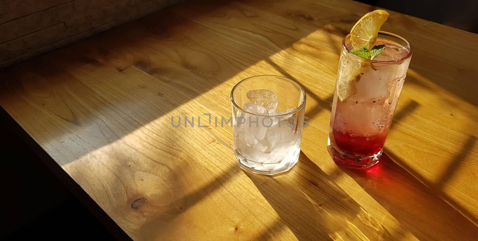 Transparent Glasses with sweet drinks inside with colorful drink, with shadow and table background with ice cubes on a bar restaurant