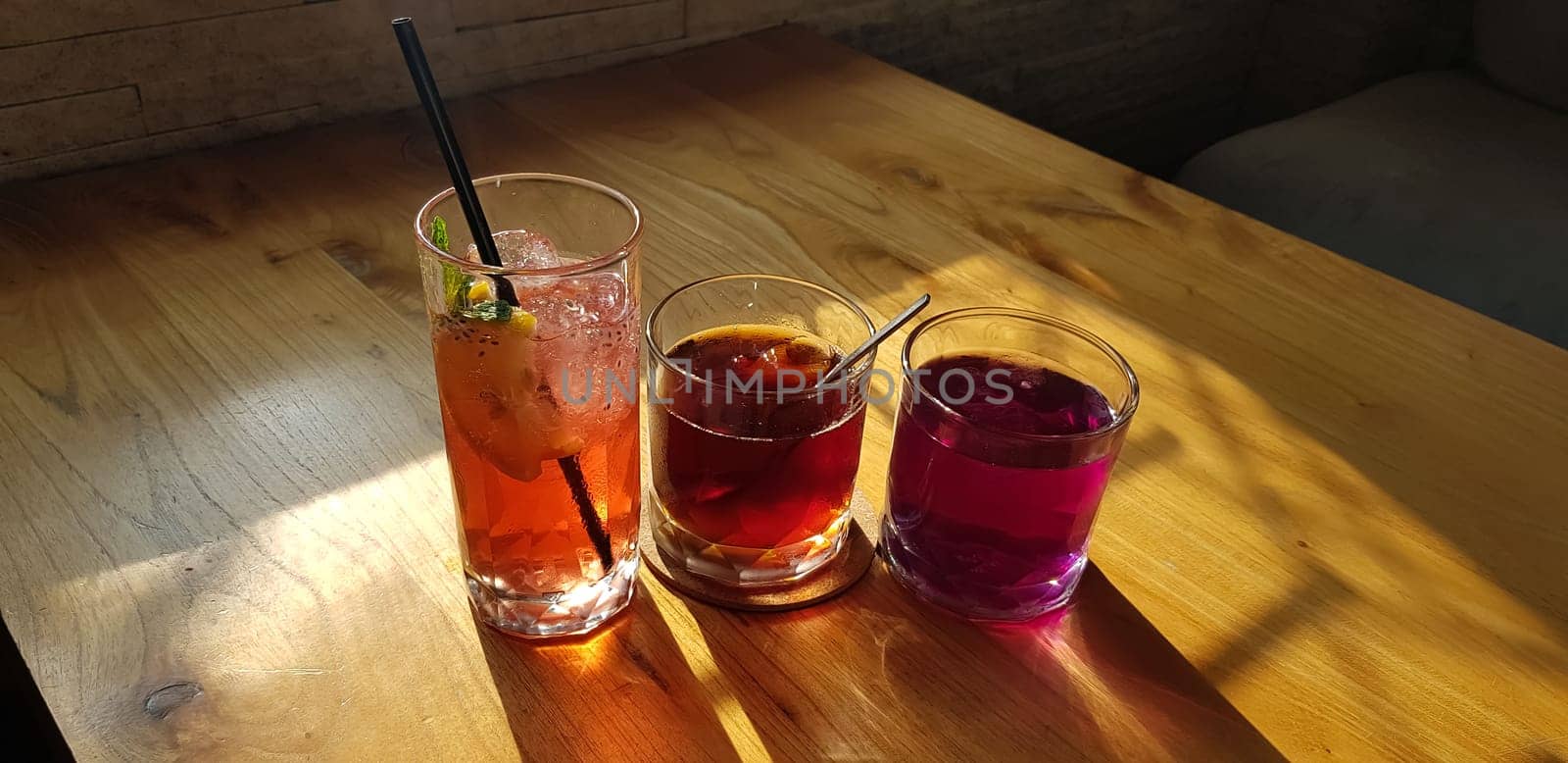 Transparent Glasses with sweet drinks inside with colorful drink, with shadow and table background with ice cubes on a bar restaurant