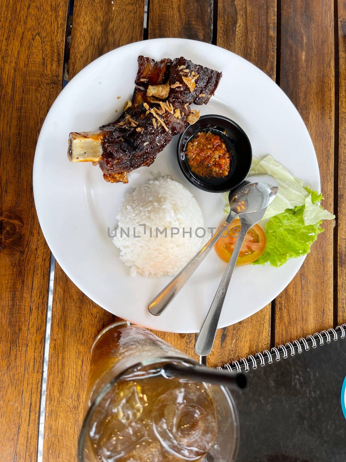 Spicy hot grilled honey roasted spare ribs from summer BBQ served with hot chili paste and rice also ice tea served in white plate