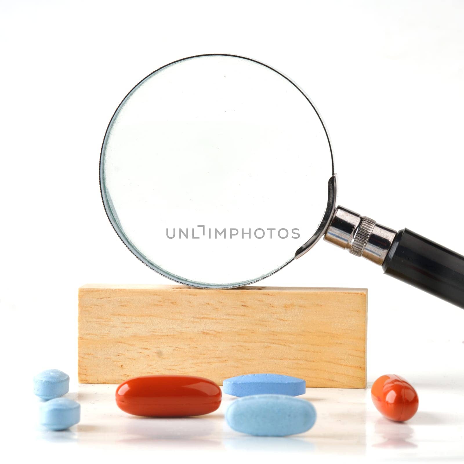 Magnifying glass on a wooden bar in close-up with pills in the foreground. A place to c