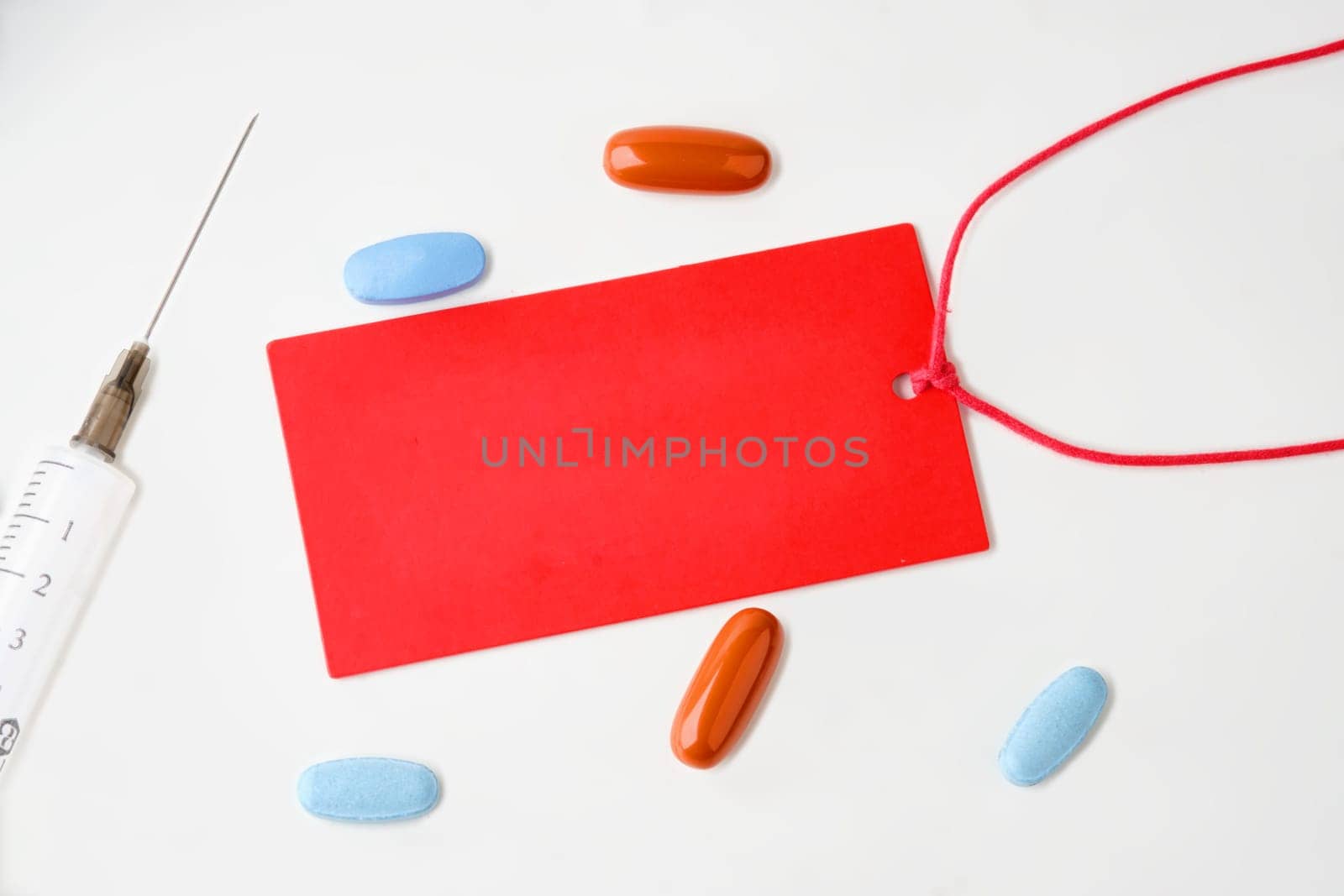 A red card on a white background. There are pills and a syringe nearby. A place to copy. Concept photo