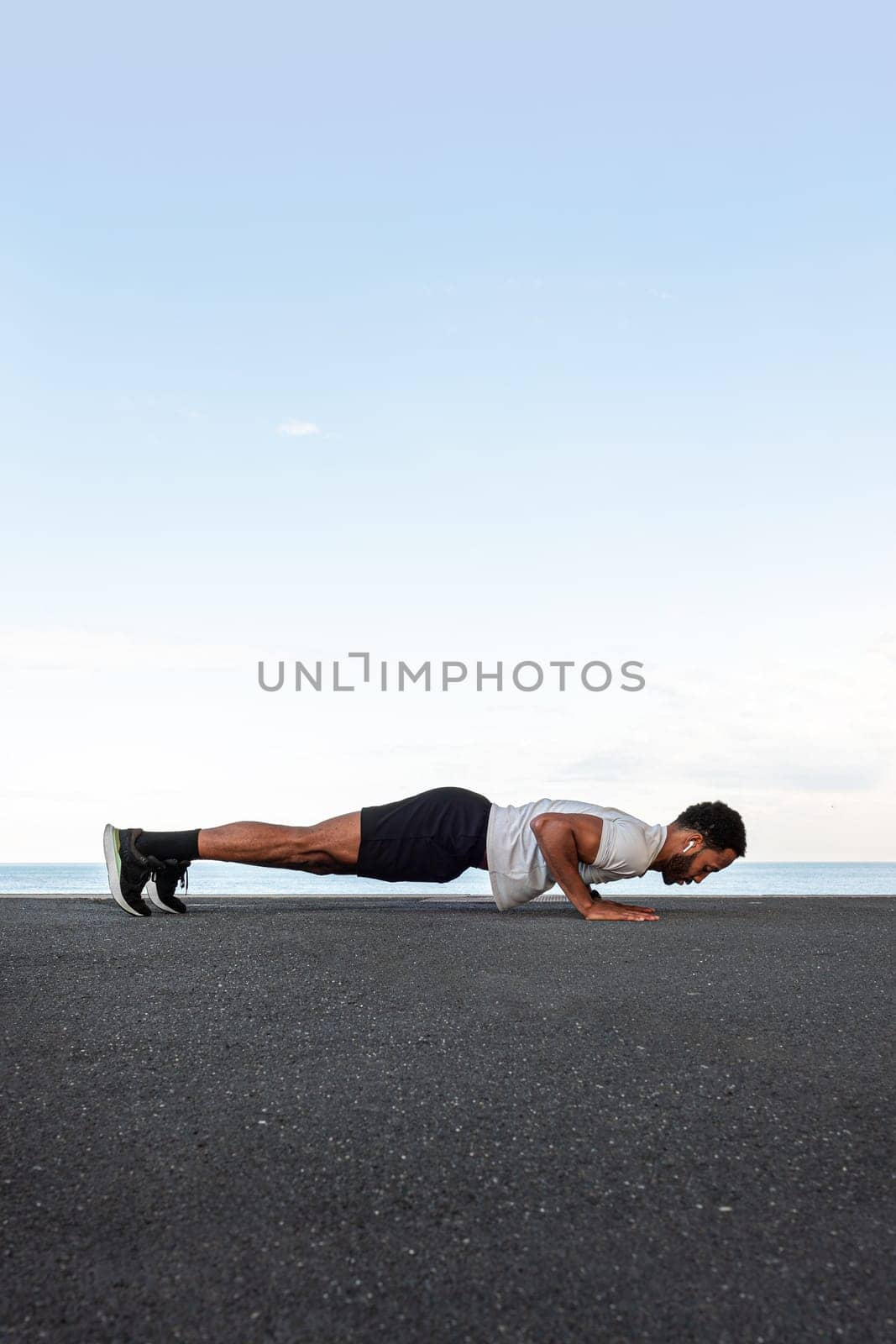 African American man doing push ups outdoors. Copy space. Vertical. by Hoverstock