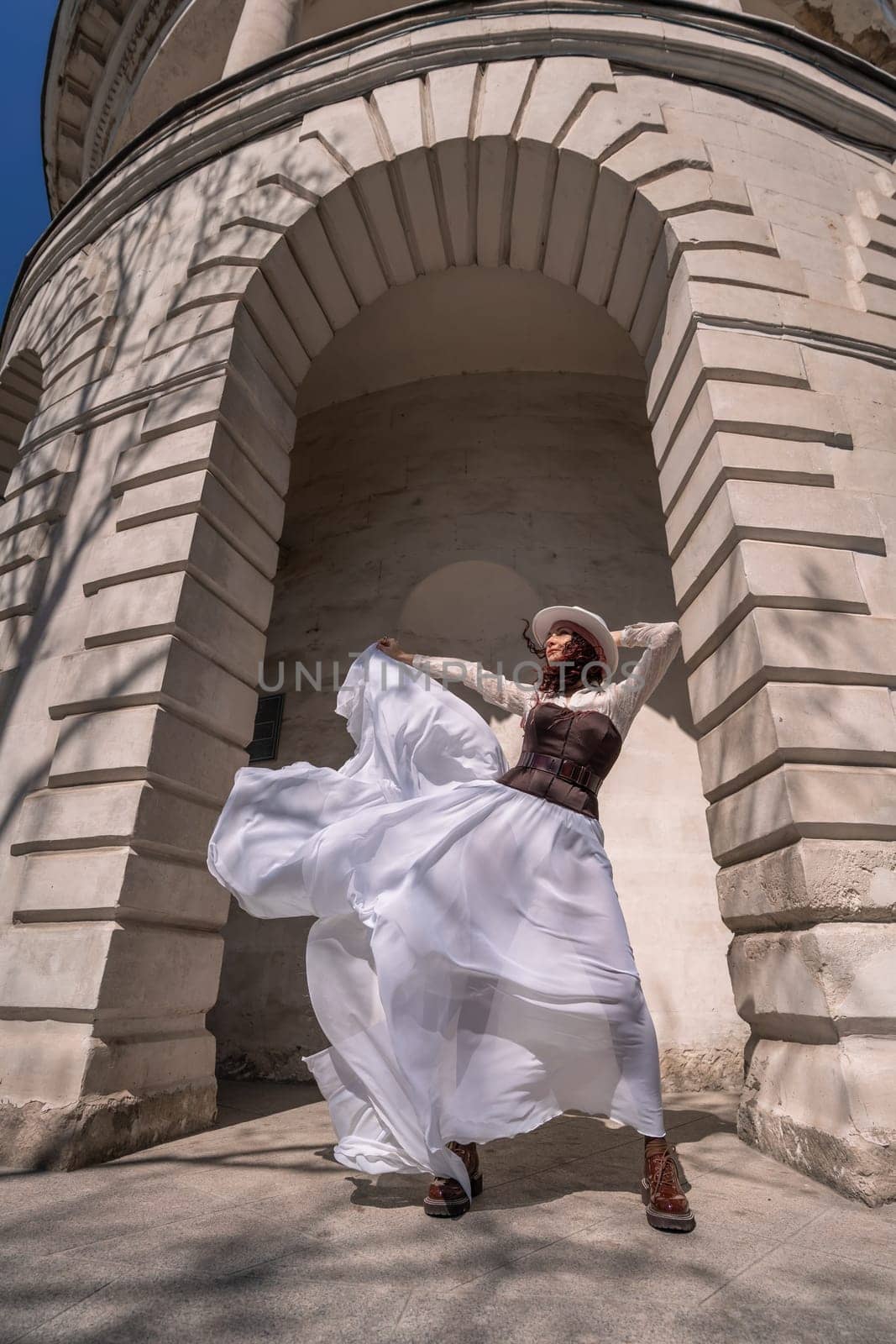 Stylish woman building city. A dancer in a long white skirt dances in front of a building with an arch. The skirt develops in the wind. by Matiunina