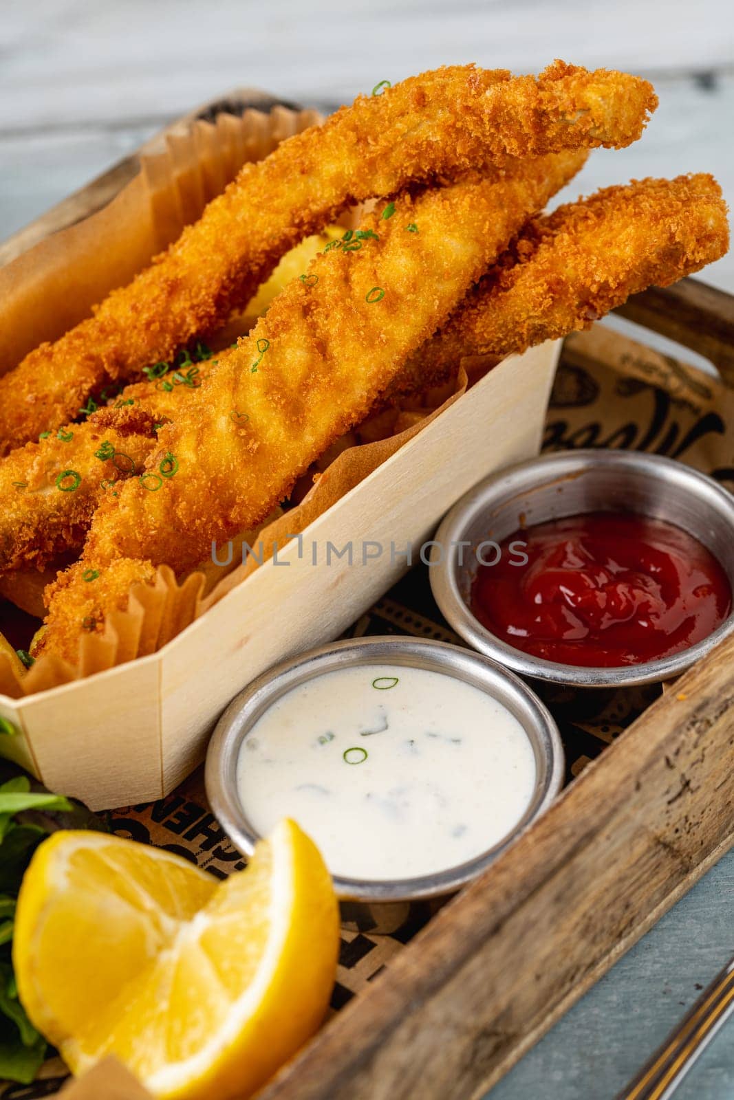 Fish and chips with fresh greens and sauces on wooden table by Sonat