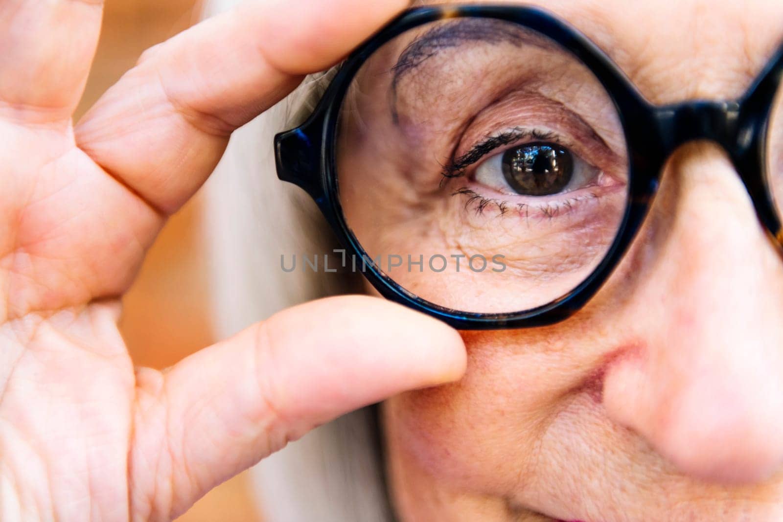 close up of the eye of a senior woman putting on glasses looking at camera, concept of eye health in elderly people and active lifestyle