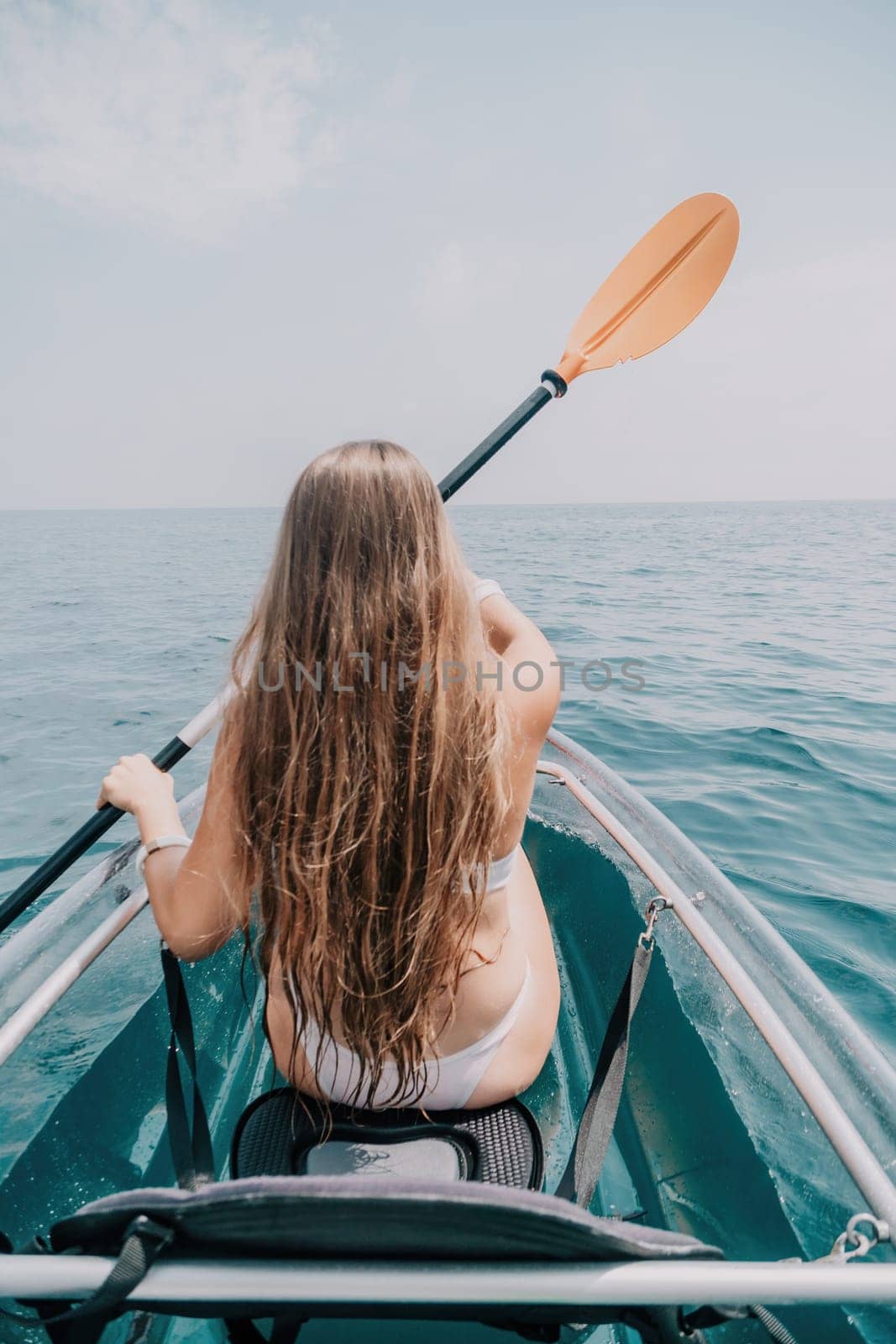 Woman in kayak back view. Happy young woman with long hair floating in transparent kayak on the crystal clear sea. Summer holiday vacation and cheerful female people having fun on the boat.