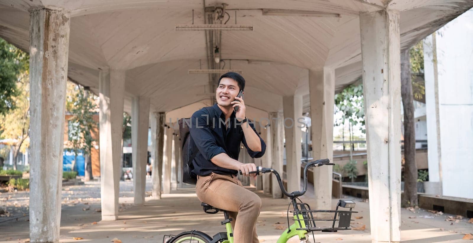 A young Asian businessman rides a bicycle to work. Standing outside the office talking on the phone and talking about business. Concept of reducing energy and reducing air pollution..