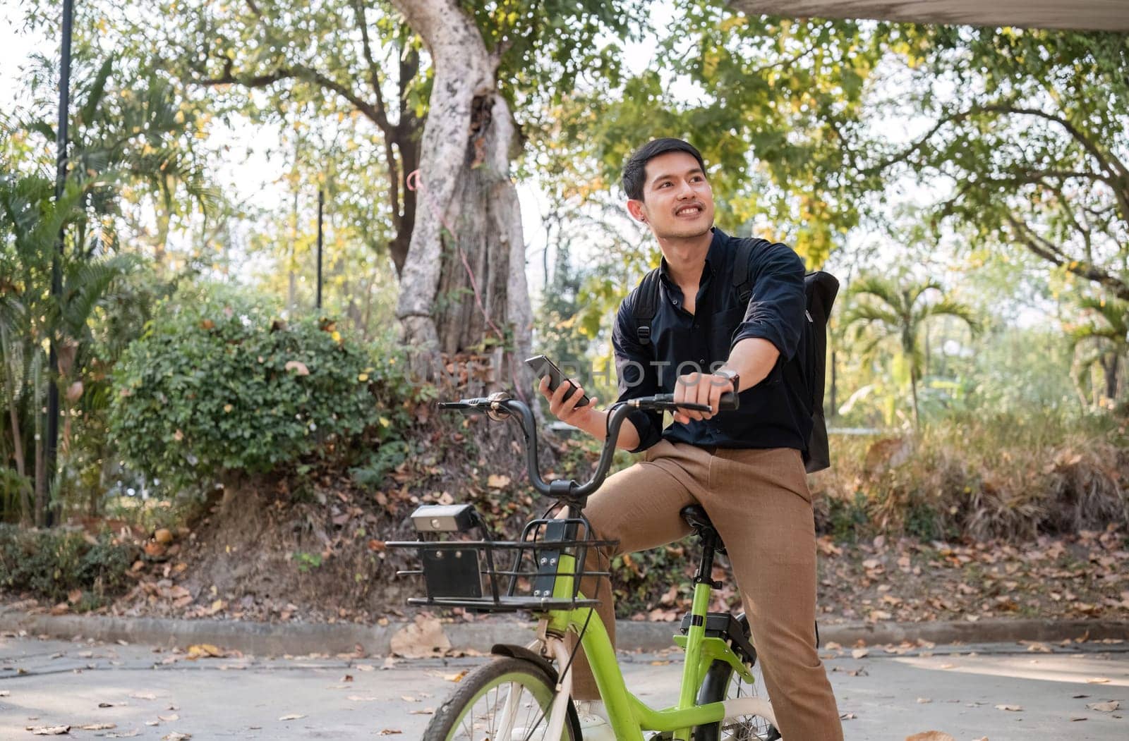 A young Asian businessman rides a bicycle to work. Standing outside the office talking on the phone and talking about business. Concept of reducing energy and reducing air pollution..