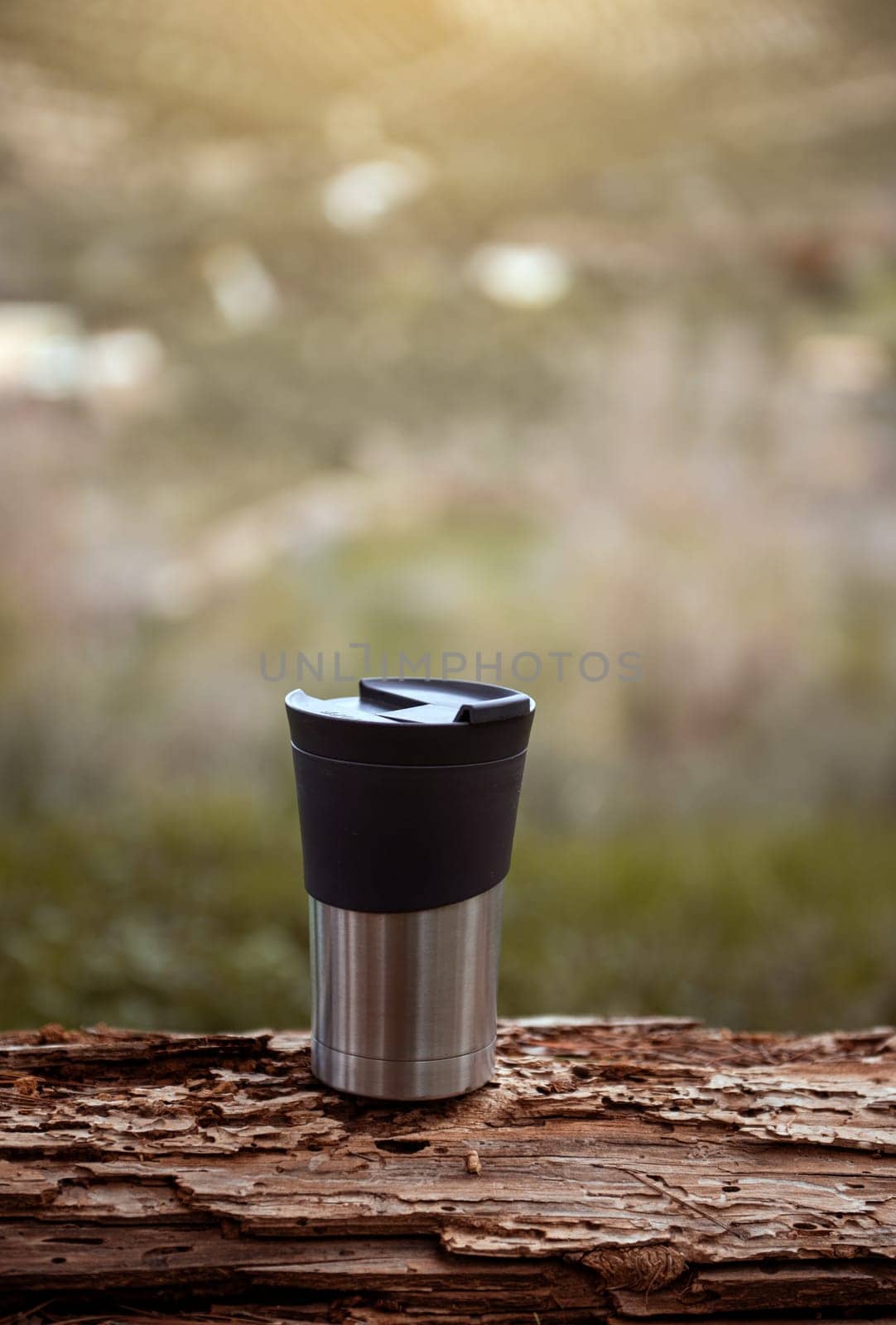 Vertical shot of a travel mug on a log over blurred nature background with copy advertising space by artgf