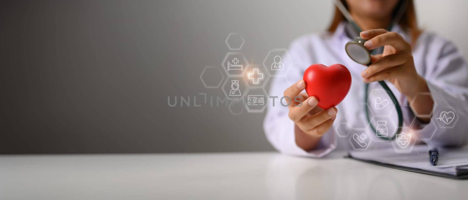 Hands of female cardiologist holding stethoscope examining red heart. Health insurance and cardiology concept by prathanchorruangsak