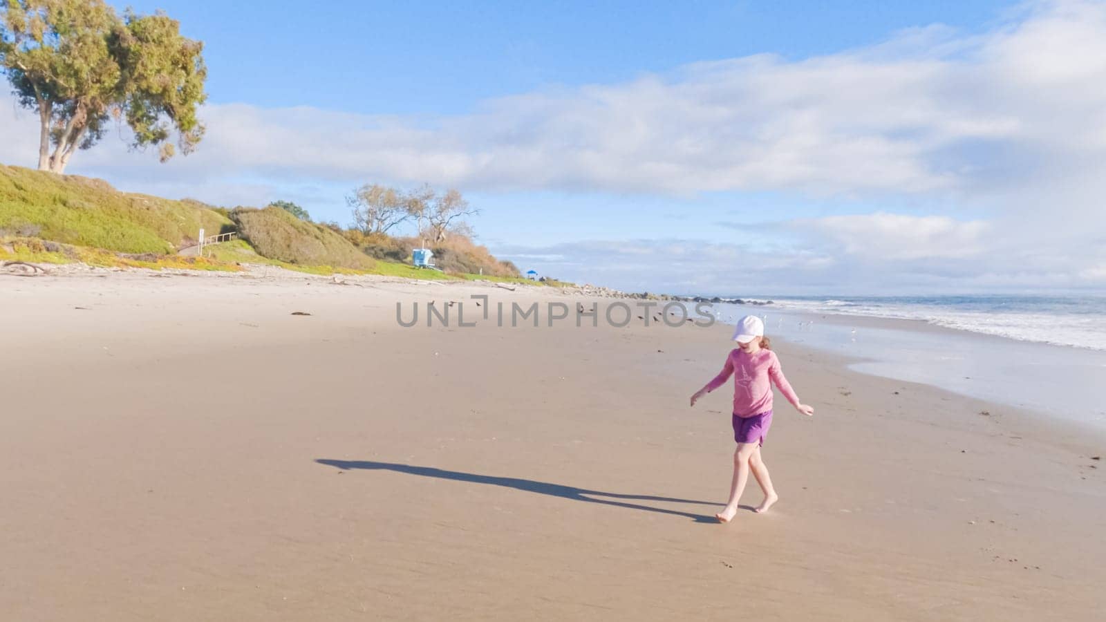 A little girl joyfully plays on the vast, empty sands of El Capitan State Beach in California during winter.