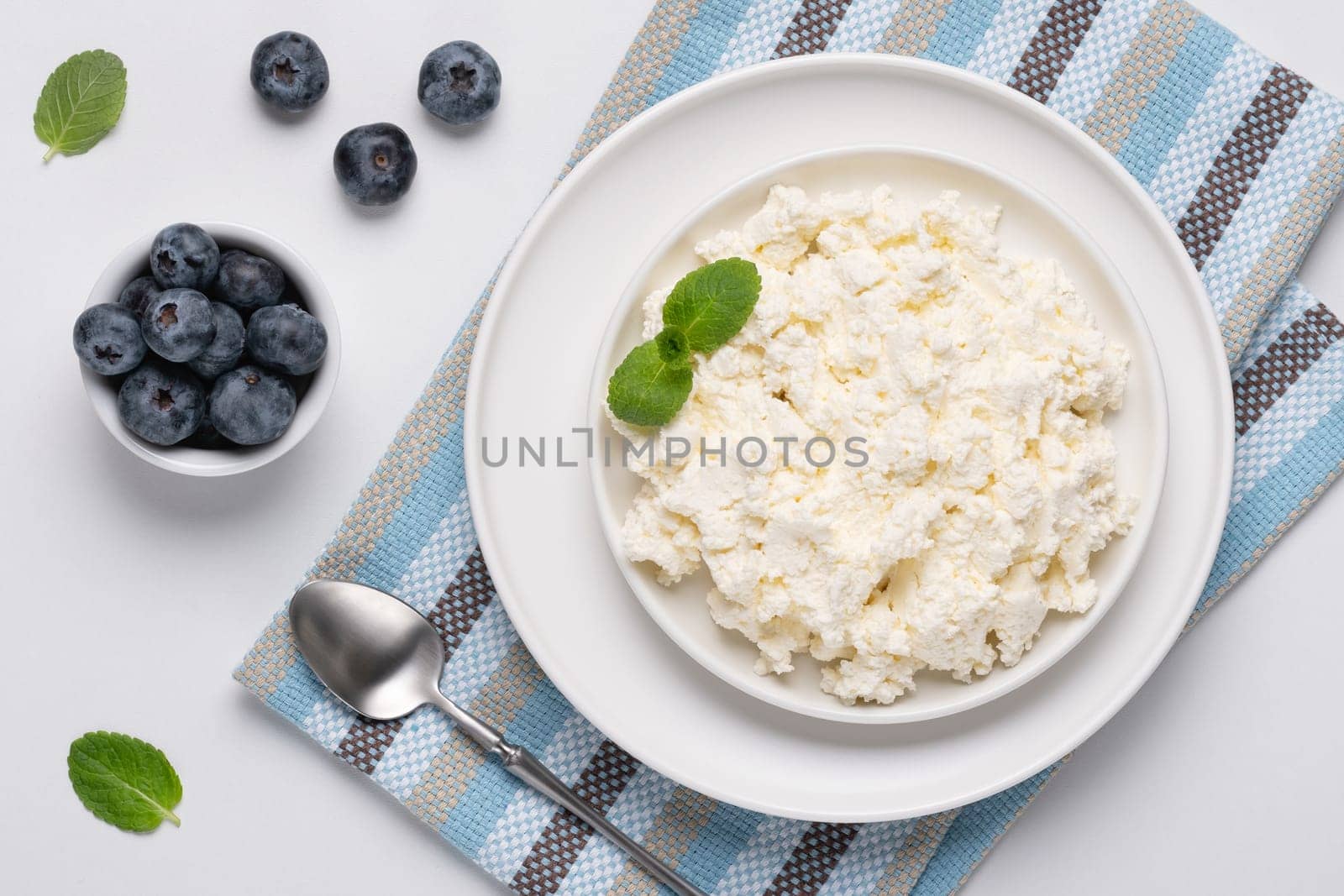 Cottage cheese with blueberry and mint on a white table. Cottage cheese in a bowl. Top view. Dairy products.