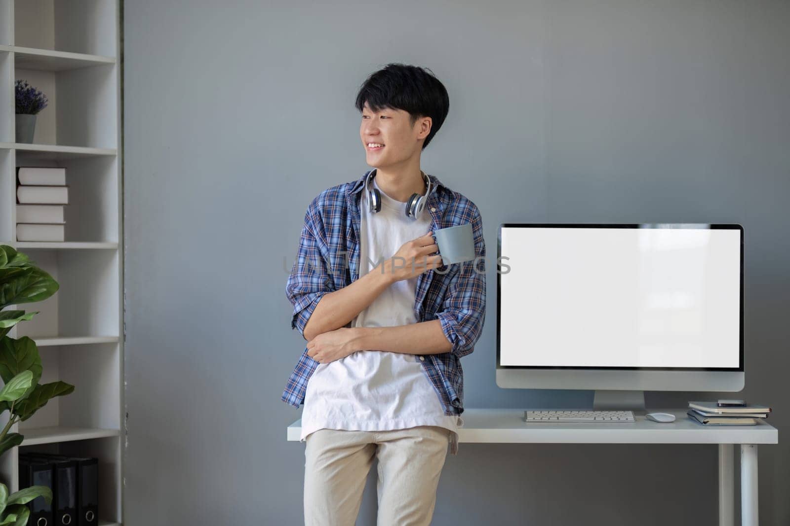 Young Asian student smiling happily at computer with blank screen on table.