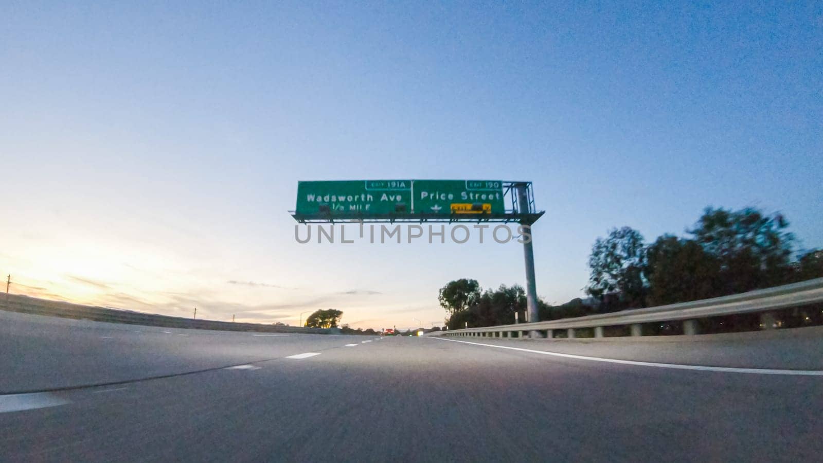 As the sun sets, driving on HWY 101 near Pismo Beach, California becomes a captivating experience with the sky painted in shades of orange and pink, casting a warm glow over the coastal landscape.