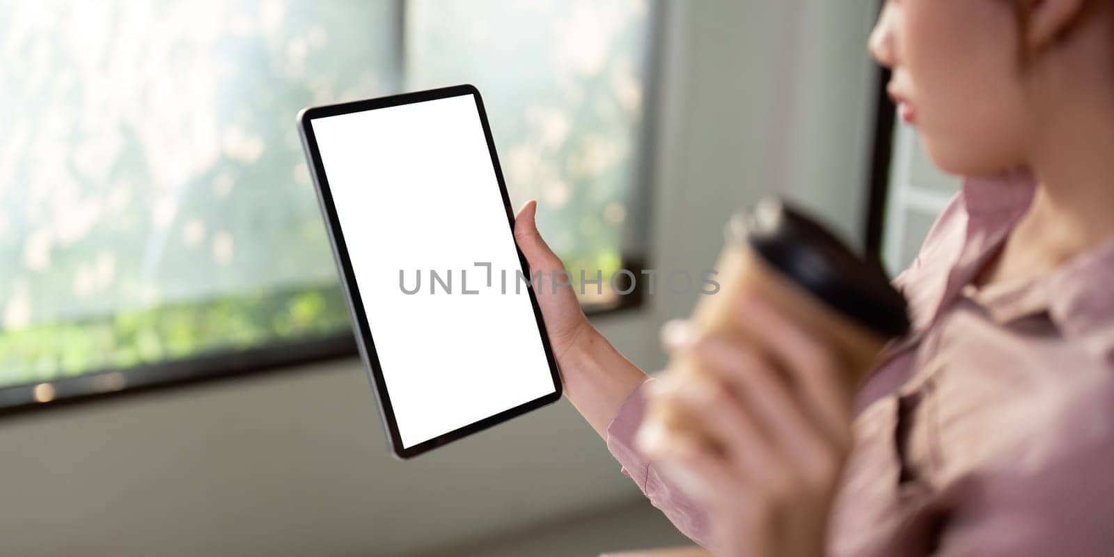 Mockup of a woman holding digital tablet with blank white desktop screen with holding a coffee cup.