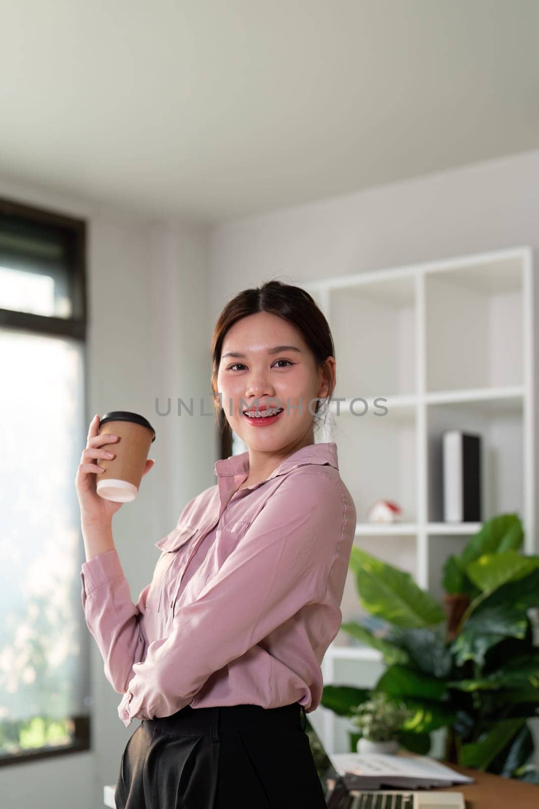 Young successful employee business woman hold takeaway craft paper cup coffee at desk at office. Achievement career concept by nateemee