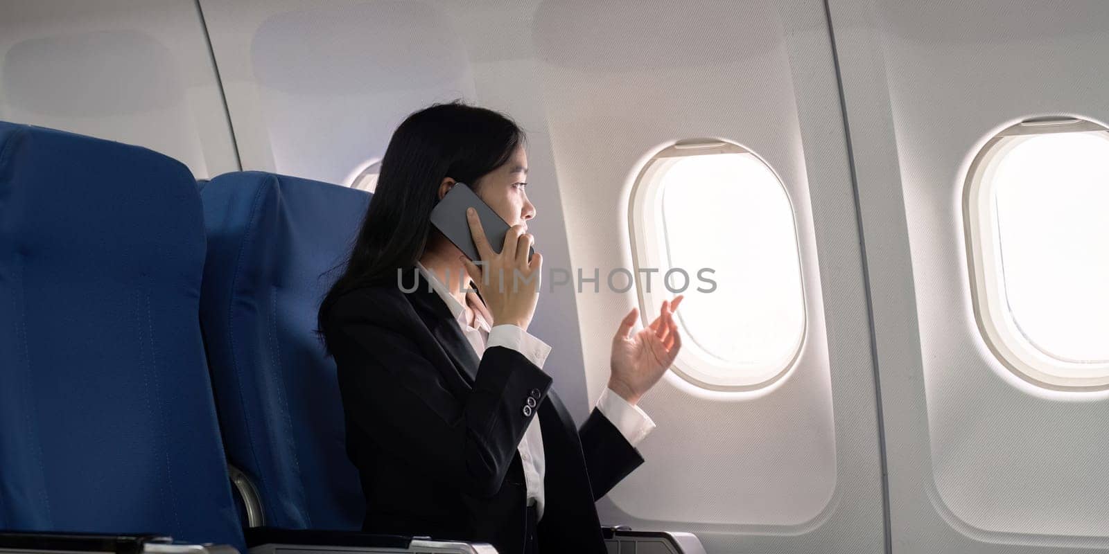 Asian young businesswoman successful or female entrepreneur in formal suit in a plane sit in a business class seat and uses a smartphone during flight. Traveling and Business concept by nateemee