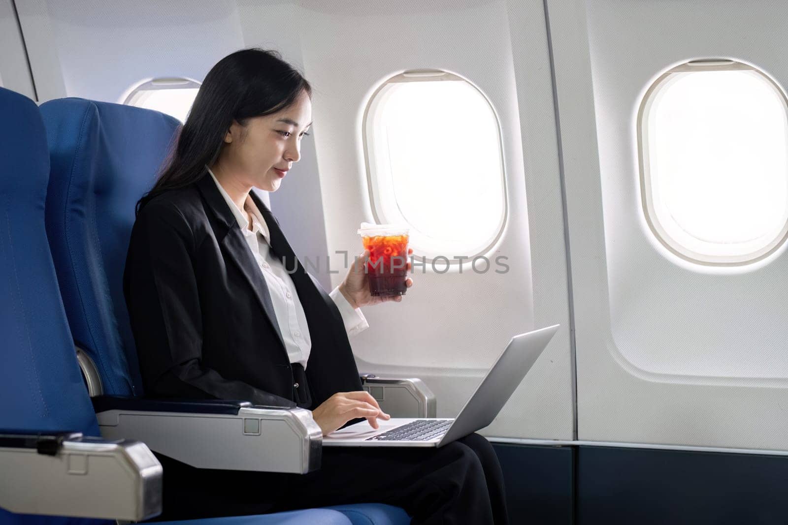 Asian young woman using laptop while drinking coffee at first class on airplane during flight, Traveling and Business concept.