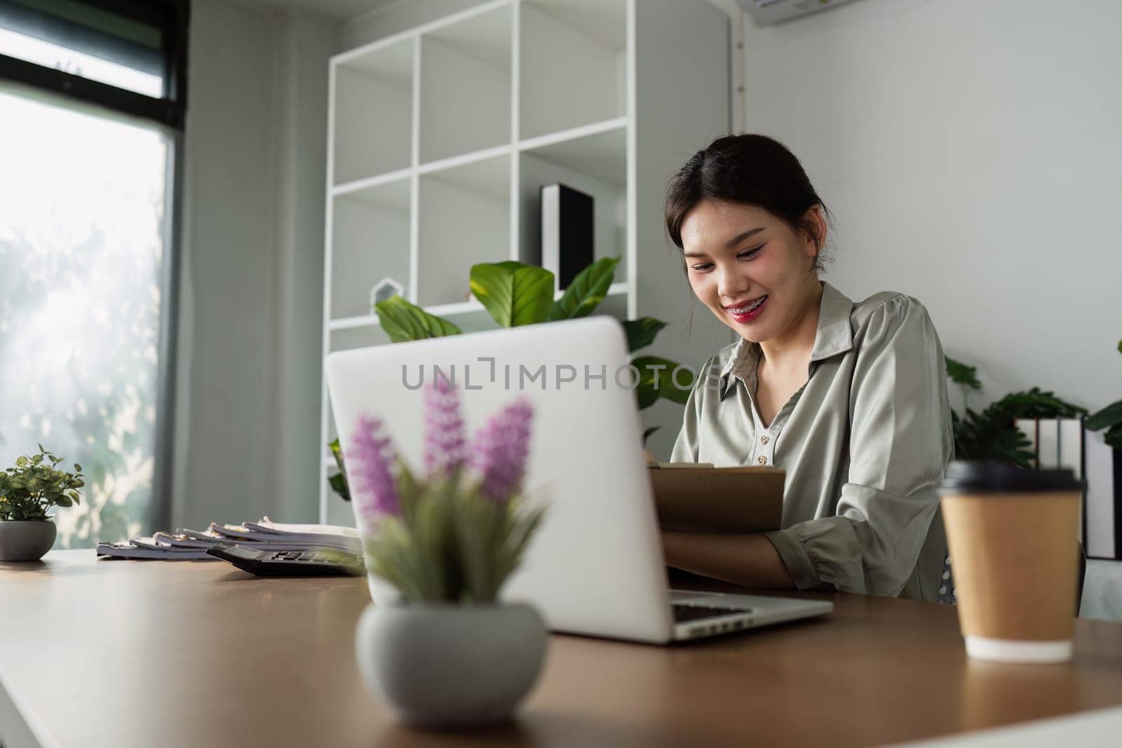 woman sitting at desk with laptop and cup of coffee, smiling and enjoying work by itchaznong