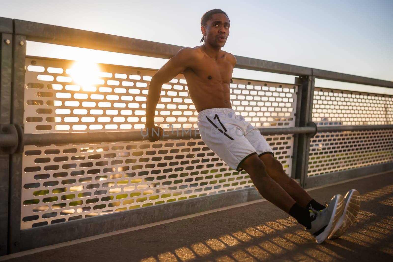 Young man is exercising on the bridge in the city. He is doing reverse push-ups.