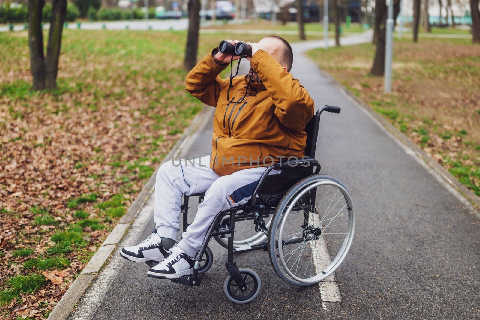 Paraplegic handicapped man in wheelchair is using binoculars outdoor. He is watching birds.