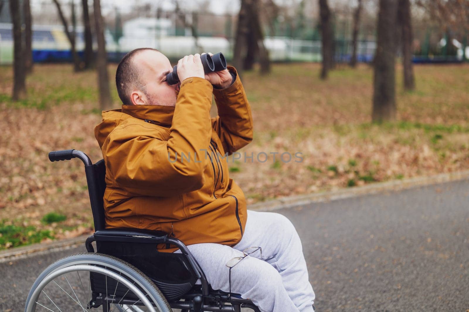 Paraplegic handicapped man in wheelchair is using binoculars outdoor. He is watching birds.