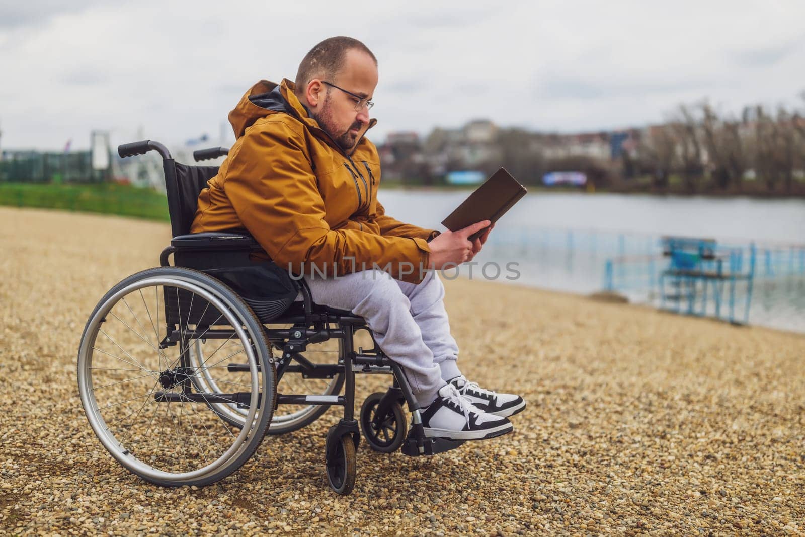 Paraplegic handicapped man in wheelchair is reading book outdoor.