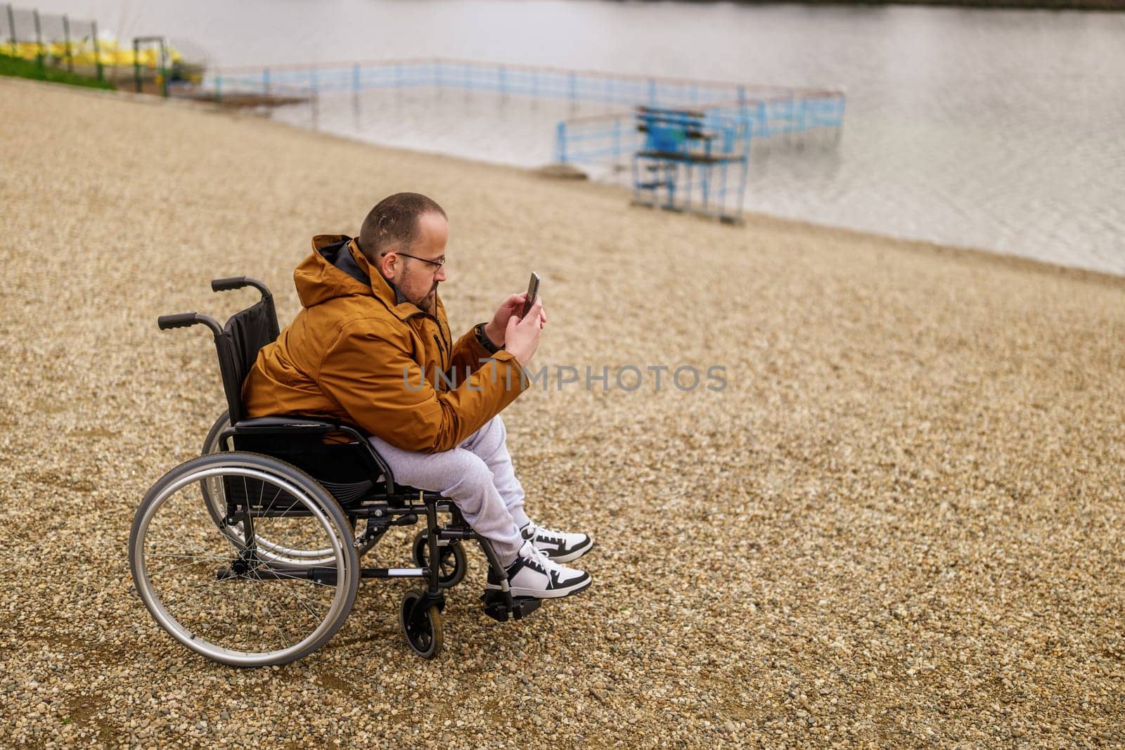 Paraplegic handicapped man in wheelchair is messaging on smartphone outdoor.