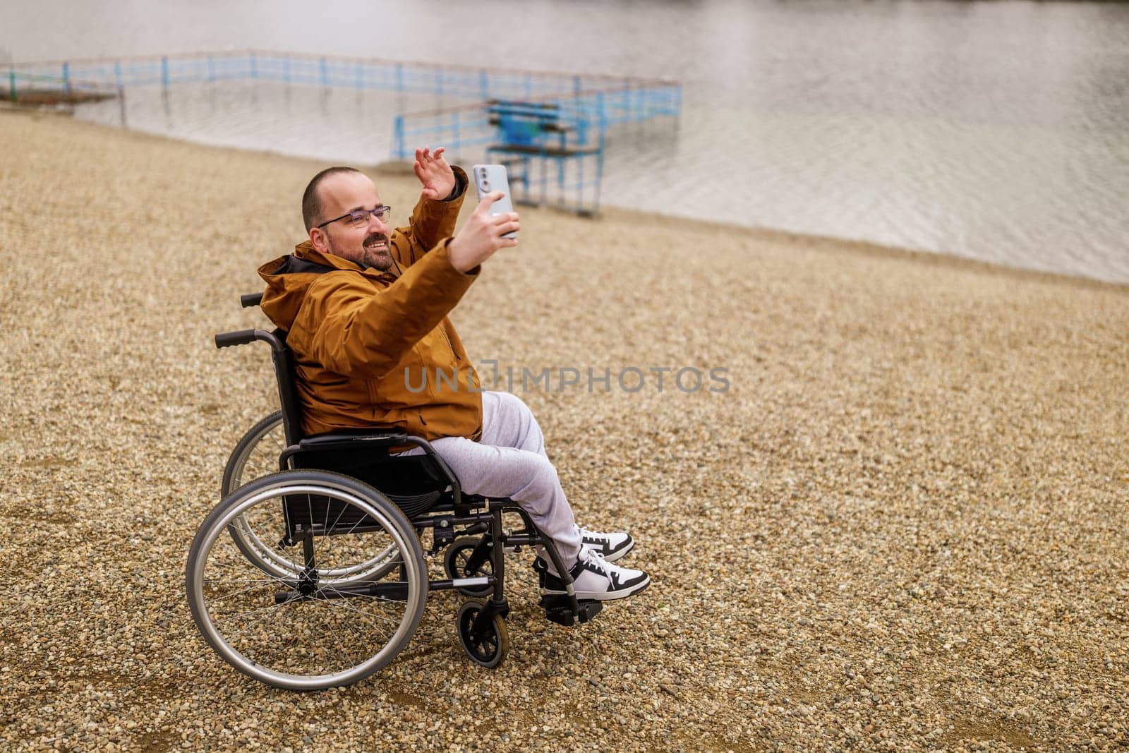 Paraplegic handicapped man in wheelchair is taking selfie with smartphone outdoor.