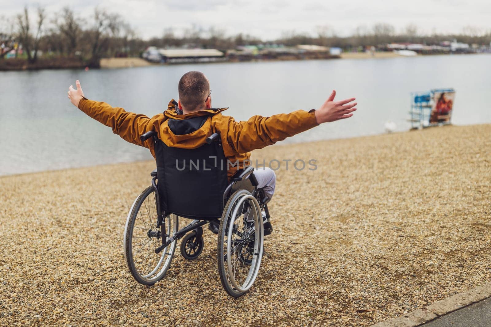 Rear view image of paraplegic handicapped man in wheelchair by the lake. He is enjoying outdoor.