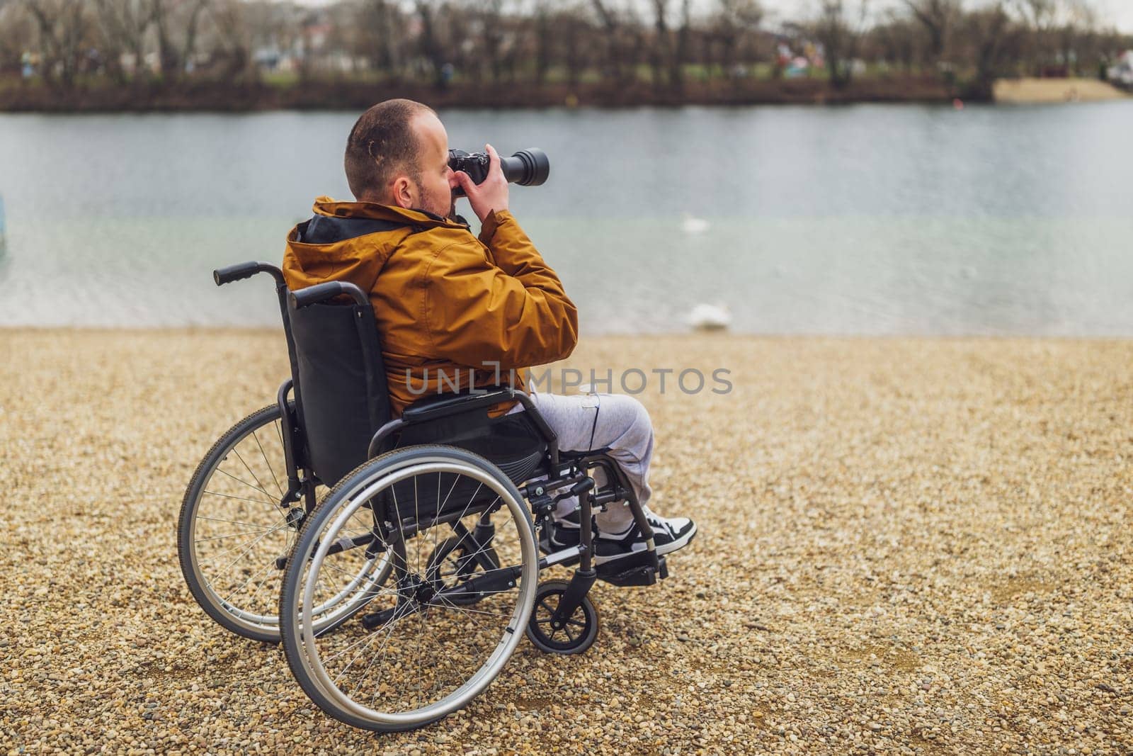 Paraplegic handicapped man in wheelchair is photographing outdoor.