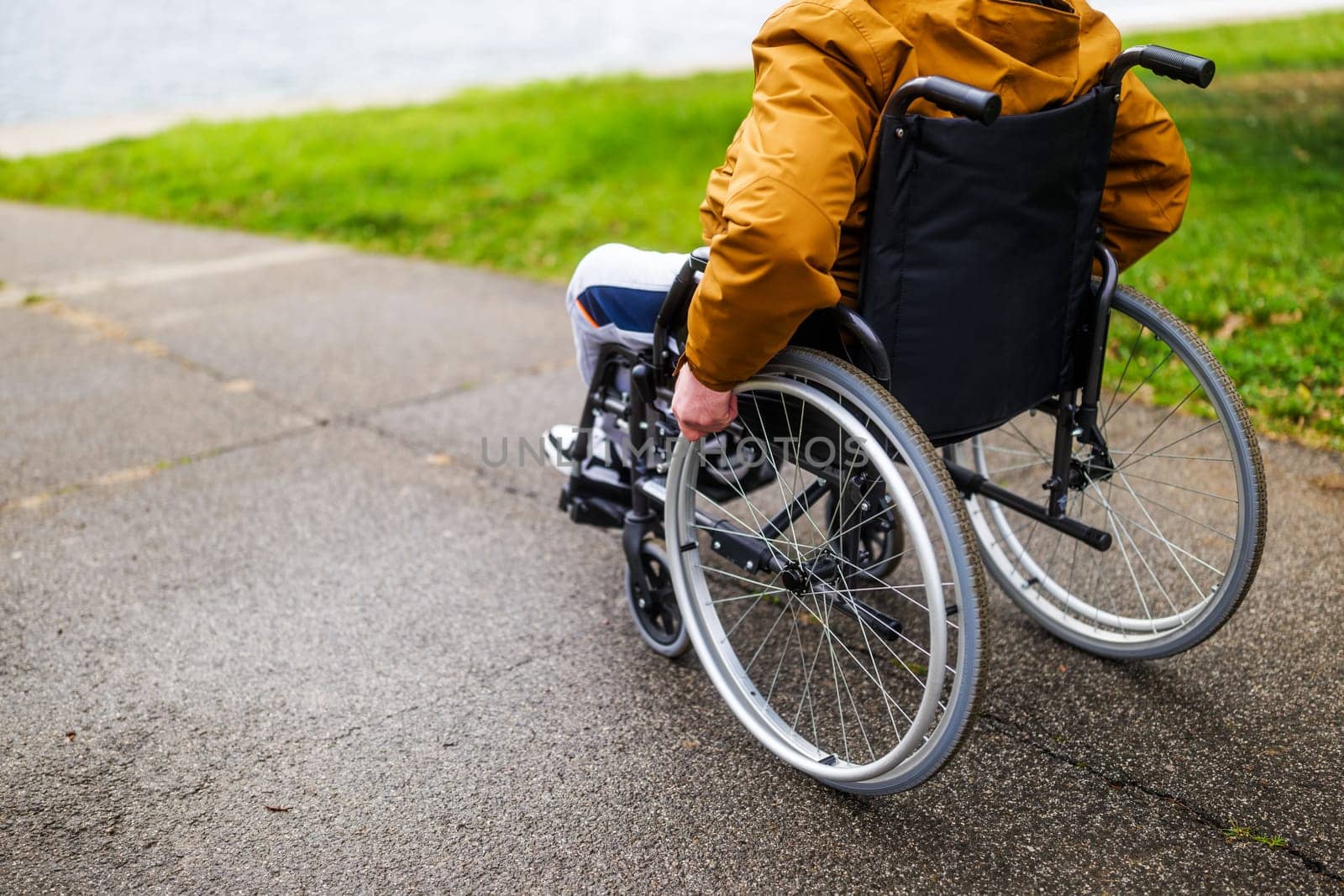 Close up image of paraplegic handicapped man in wheelchair in park. He is rolling on pathway.