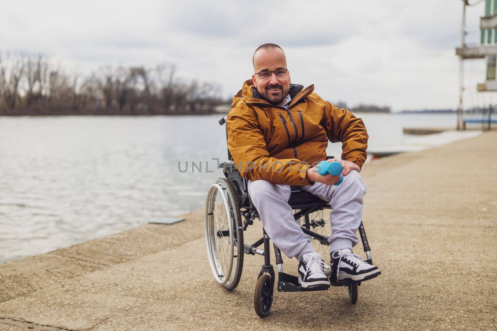 Happy paraplegic handicapped man in wheelchair by the lake. He is ready for exercise with weights.
