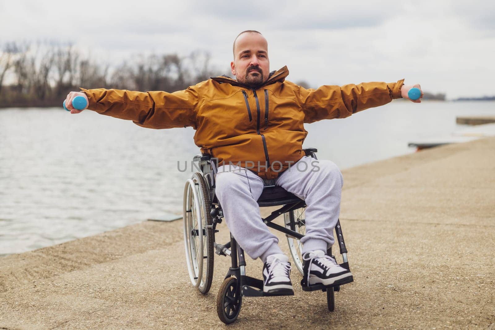 Paraplegic handicapped man in wheelchair by the lake. He is exercising with weights.