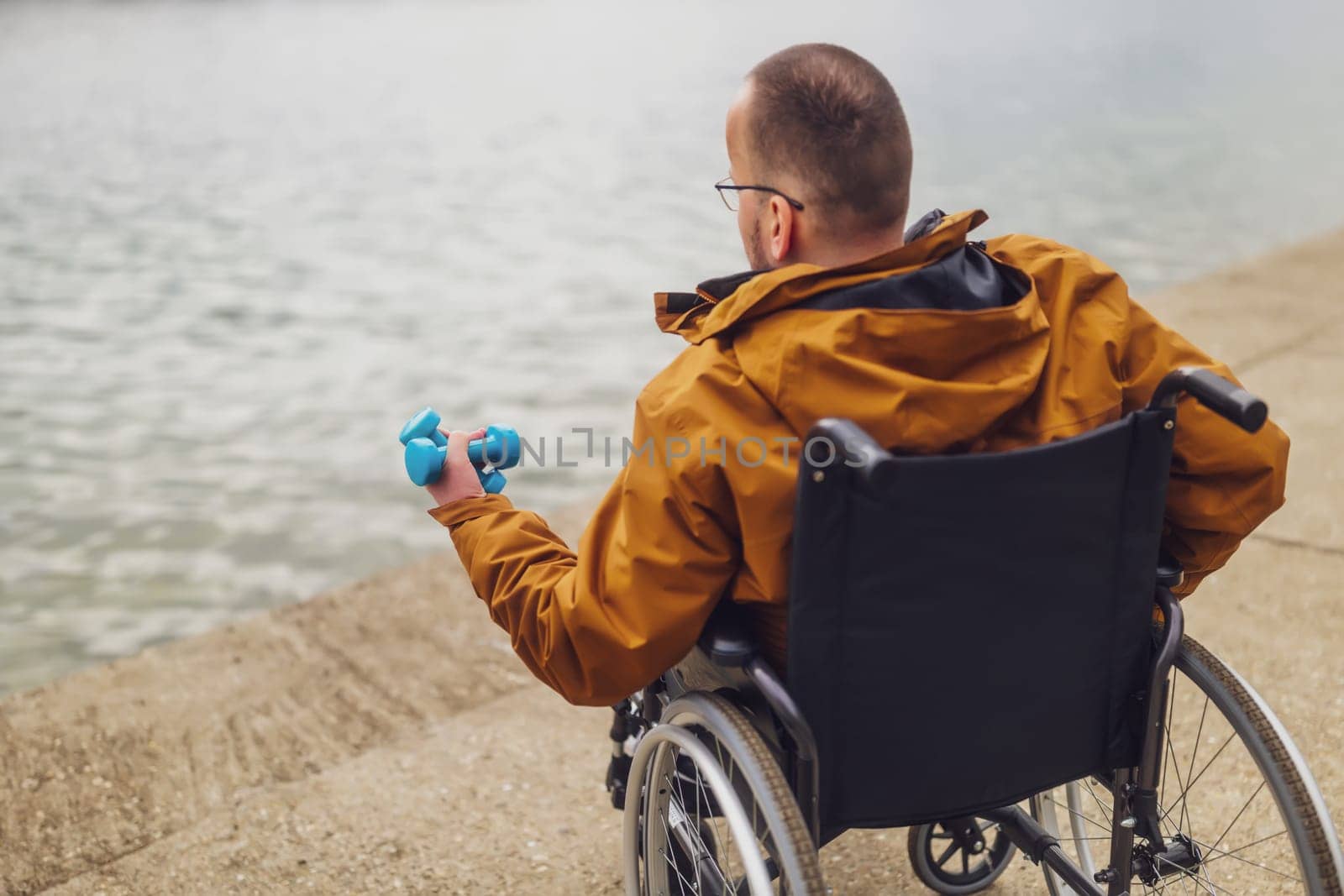 Paraplegic handicapped man in wheelchair by the lake,he is ready for exercise with weights by djoronimo