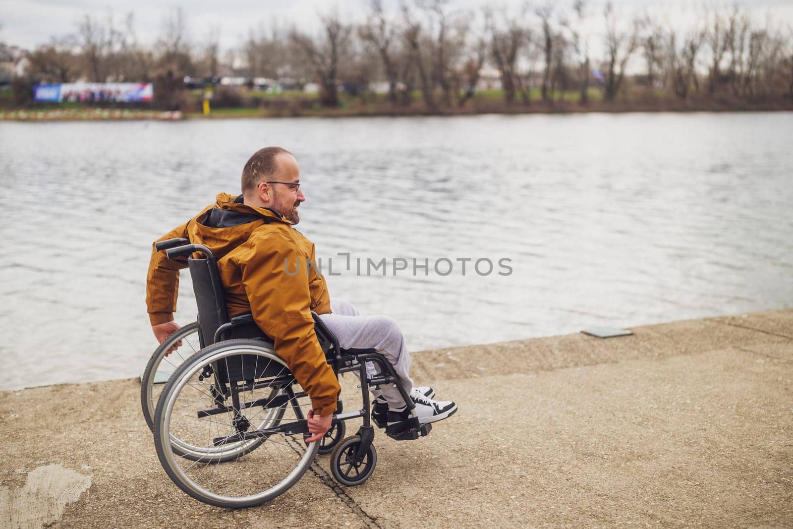 Happy paraplegic handicapped man in wheelchair by the lake. He is rolling on walkway.