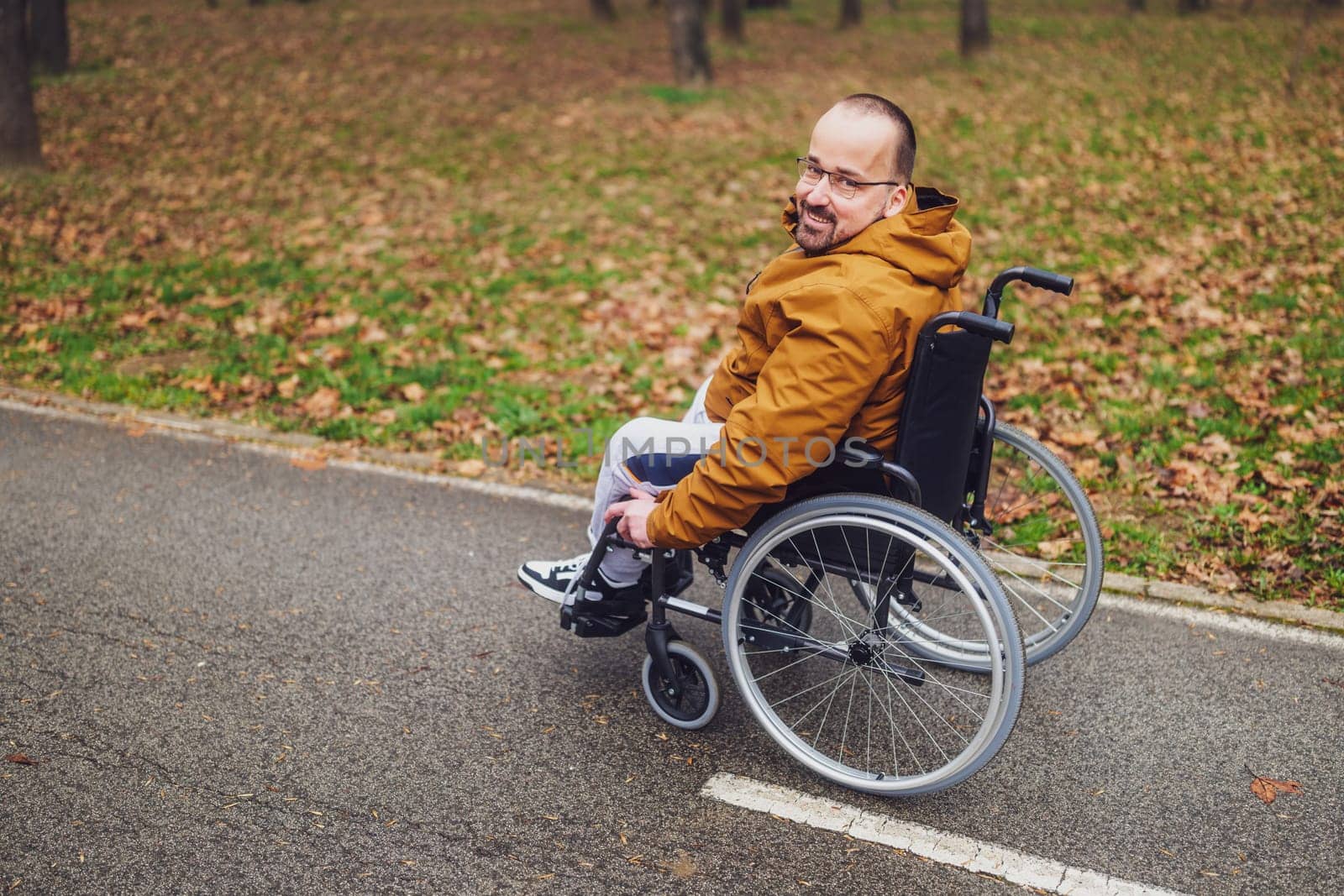 Portrait of happy paraplegic handicapped man in wheelchair in park. He is rolling on pathway.