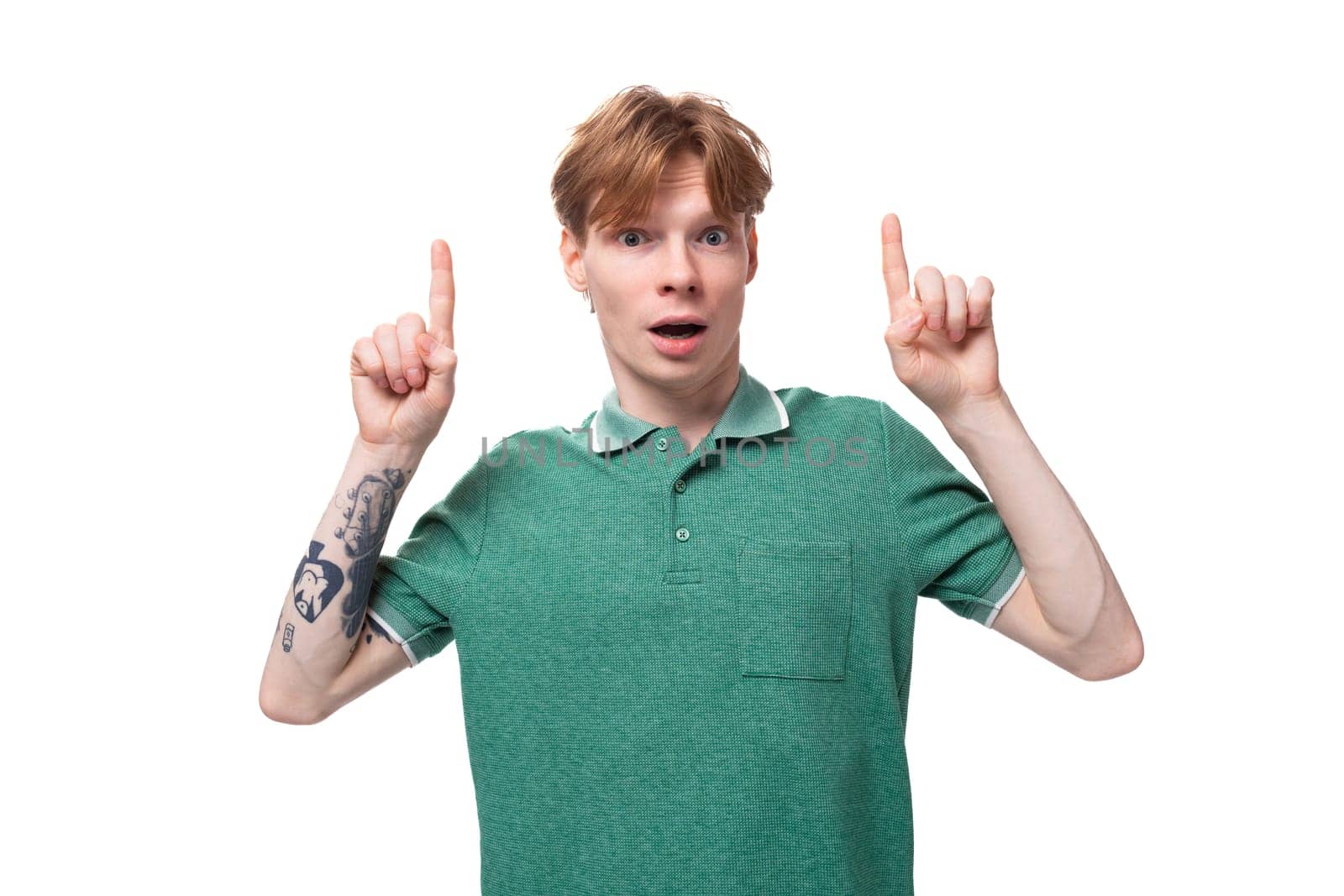 young satisfied happy european guy with red hair with a tattoo on his forearm points his finger at the space for advertising.