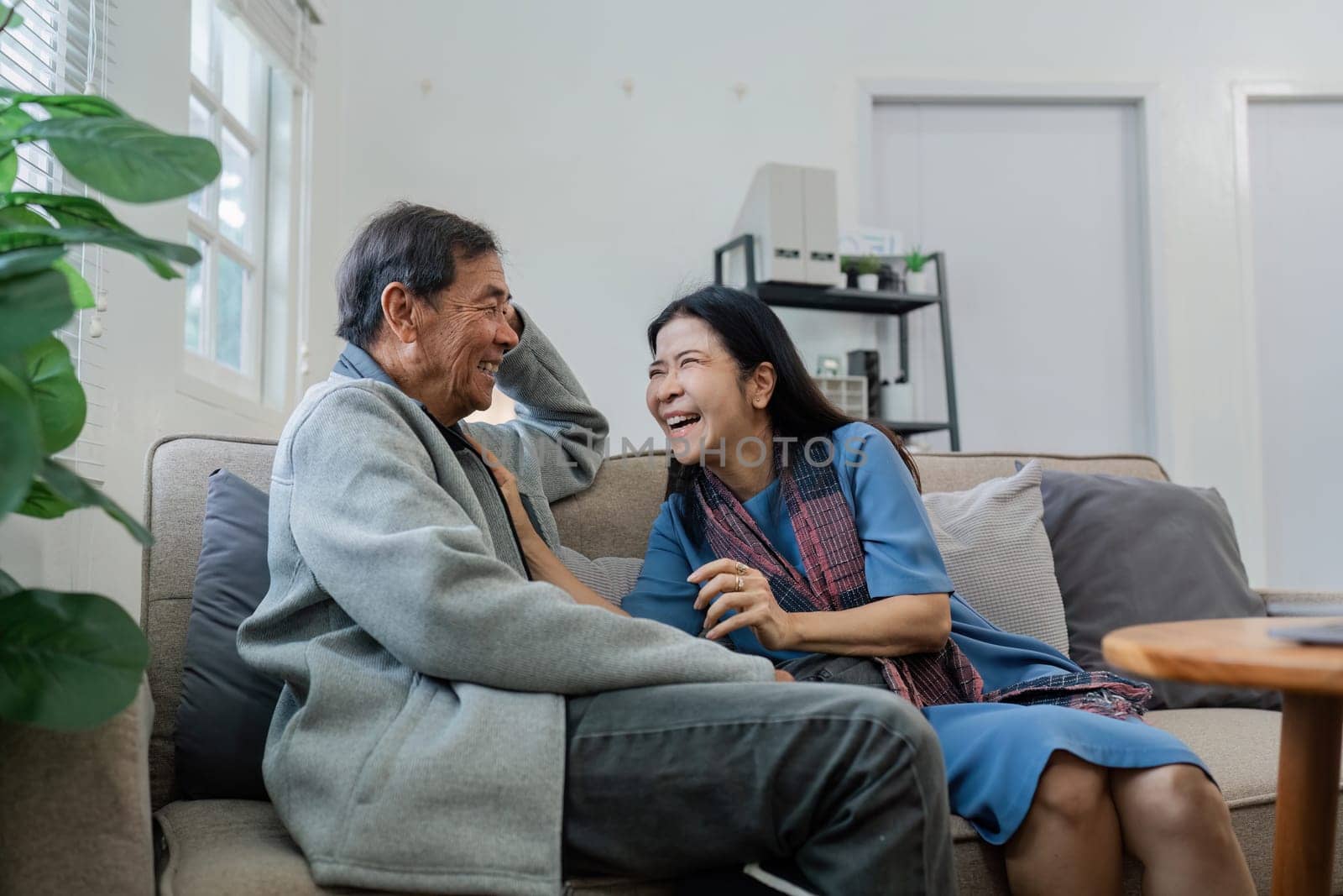 Older couples sit and chat and head over each other relaxed and happy on sofa at home on weekday in comfortable by itchaznong
