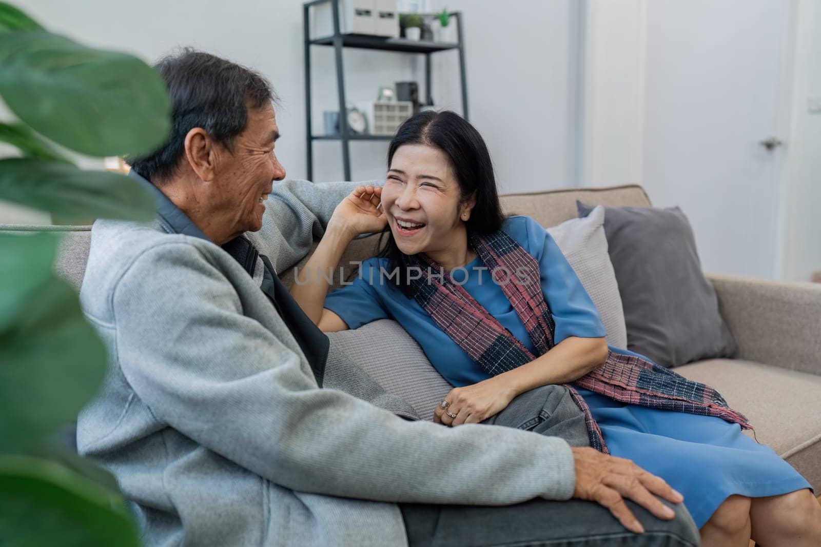 Older couples sit and chat and head over each other relaxed and happy on sofa at home on weekday in comfortable.