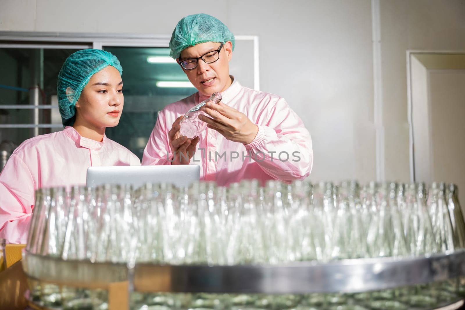 Within a beverage factory line engineers meticulously inspect product bottles on the conveyor belt. Inspection and quality control conducted by professionals using a laptop for detailed scrutiny.