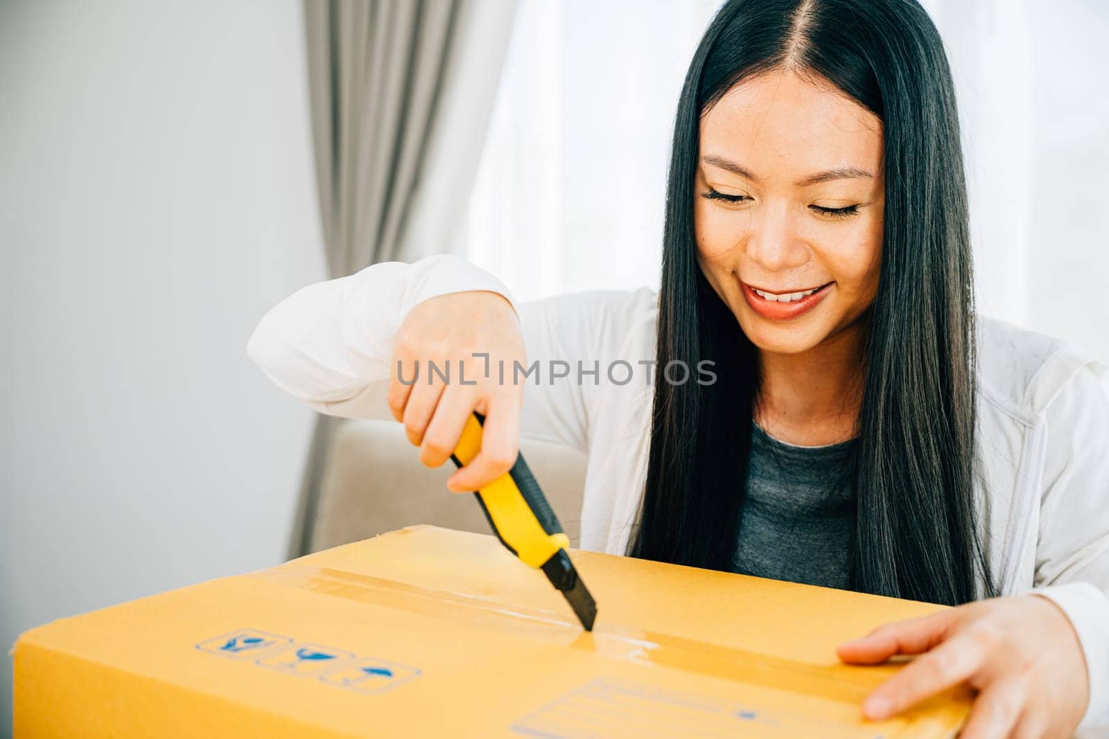 A woman holds a utility cutter for precision unboxing revealing online shopping contents by Sorapop