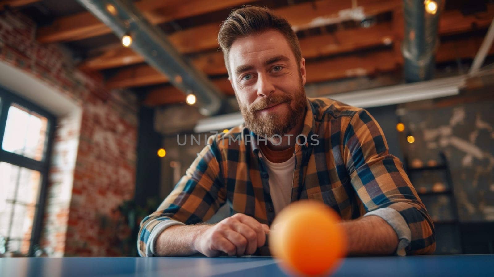 A man sitting at a ping pong table with an orange ball