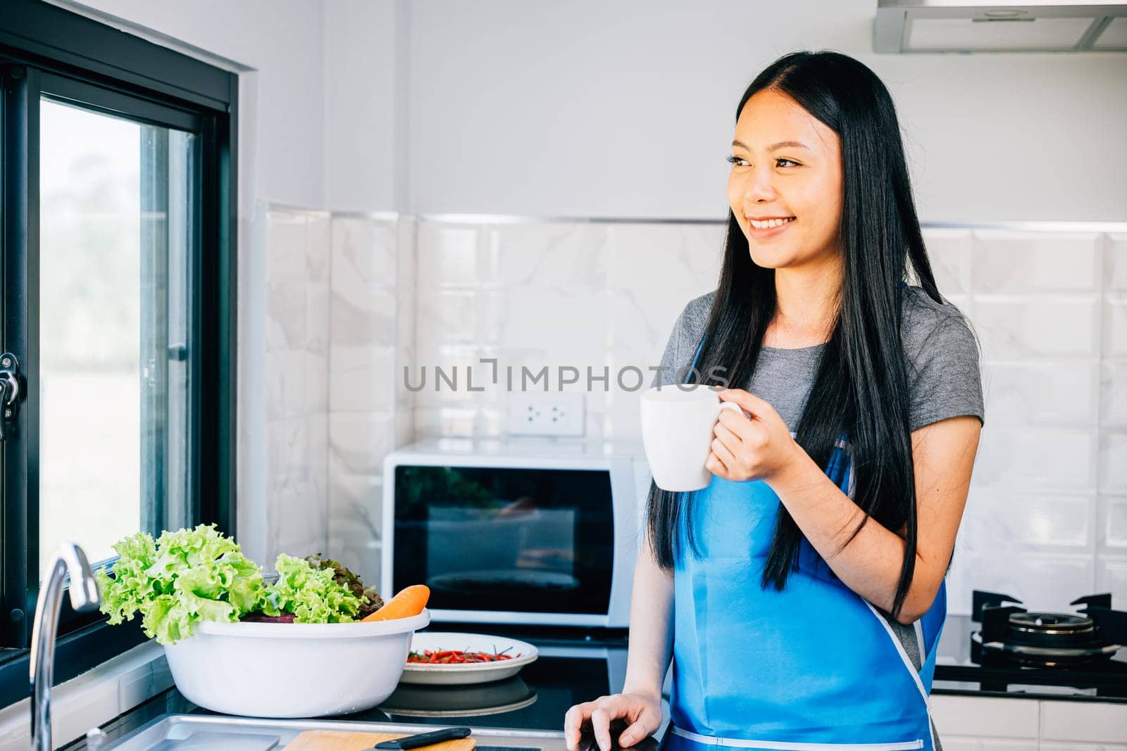 A woman enjoys her morning in a cozy kitchen holding a cup of coffee and smiling. Illustrating a carefree cheerful moment while savoring a hot drink at home.