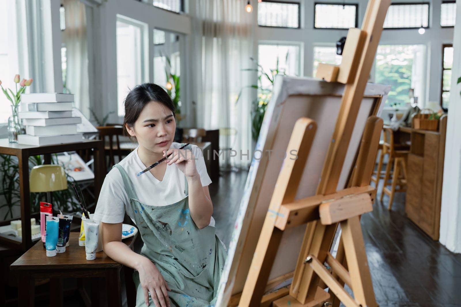 beautiful young woman artist working on painting something on a large canvas by itchaznong