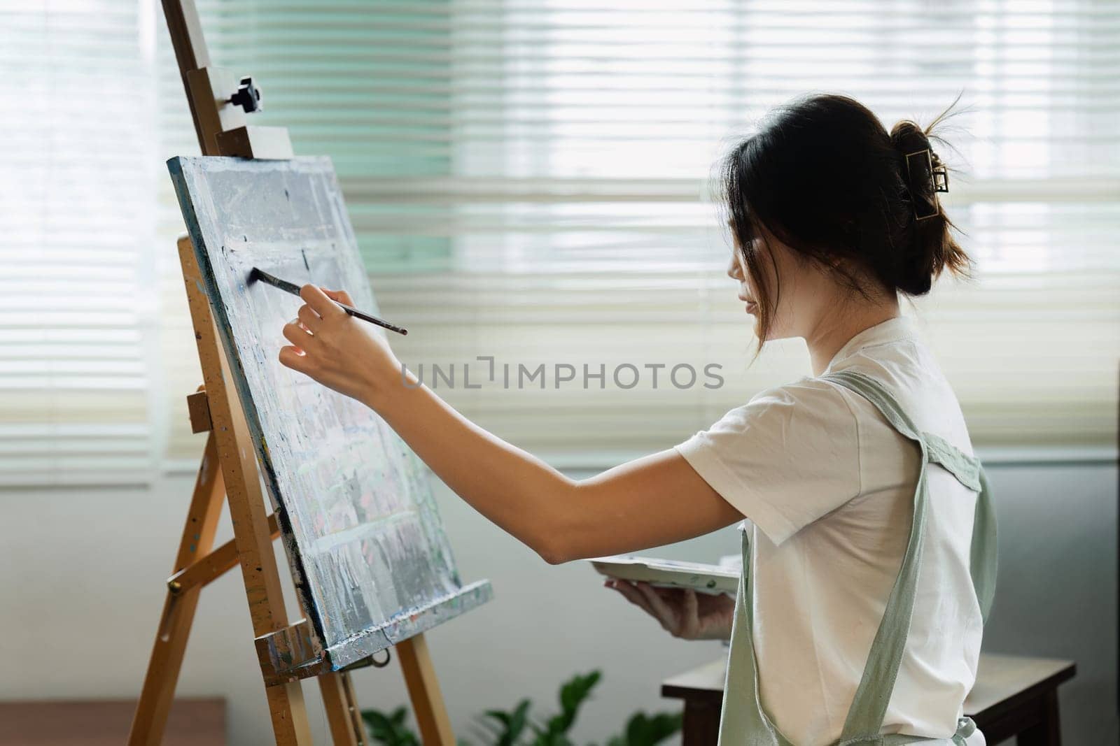 beautiful young woman artist working on painting something on a large canvas by itchaznong