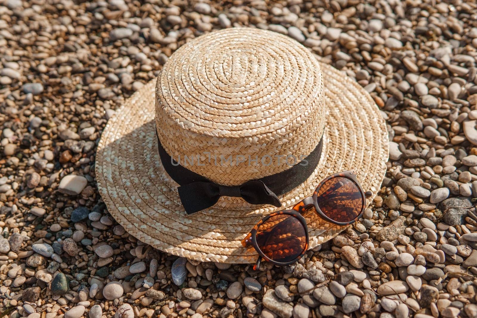 A straw hat and sunglasses on the beach. Pebbles on the seashore, close-up. The natural background.